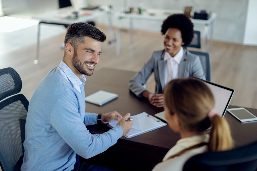 Happy man talking to his wife before signing a contract with insurance agent during the meeting in the office.